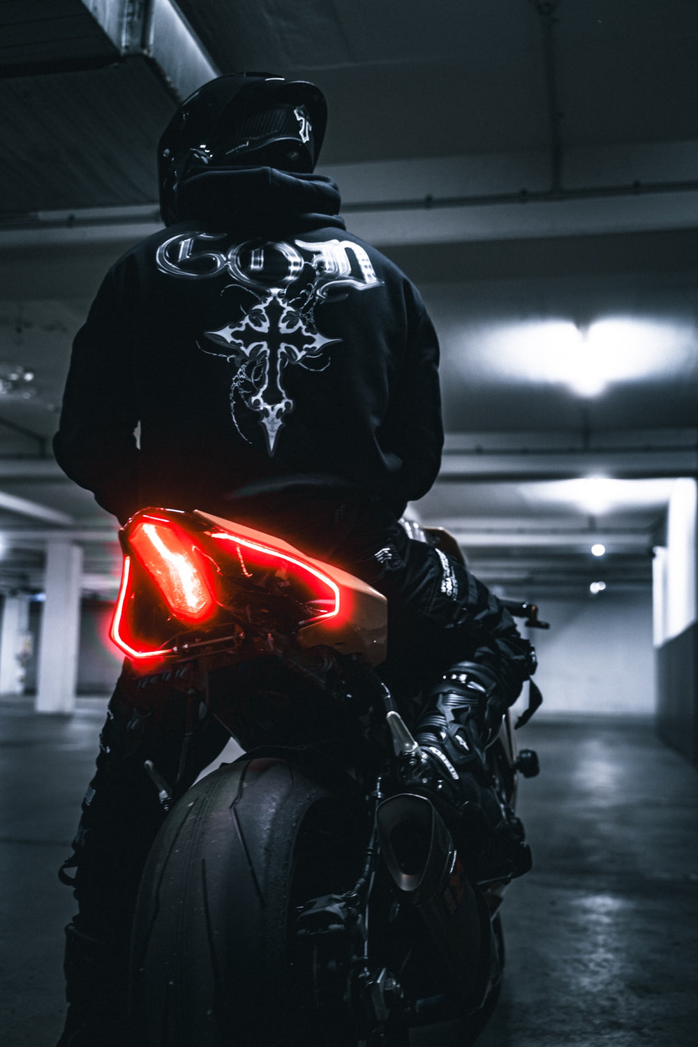 Hurt.Biker rider in GOD hoodie, red taillight, parking garage